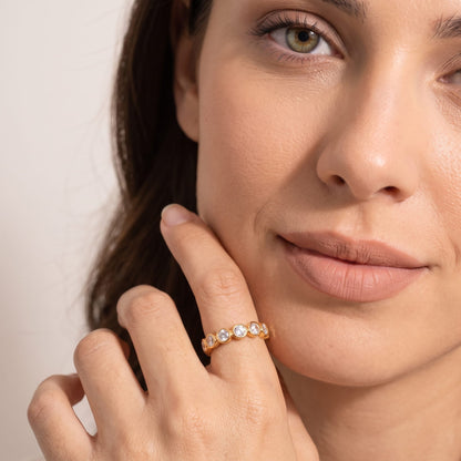 Woman wearing the Ariana round eternity gold ring on the hand touching her chin