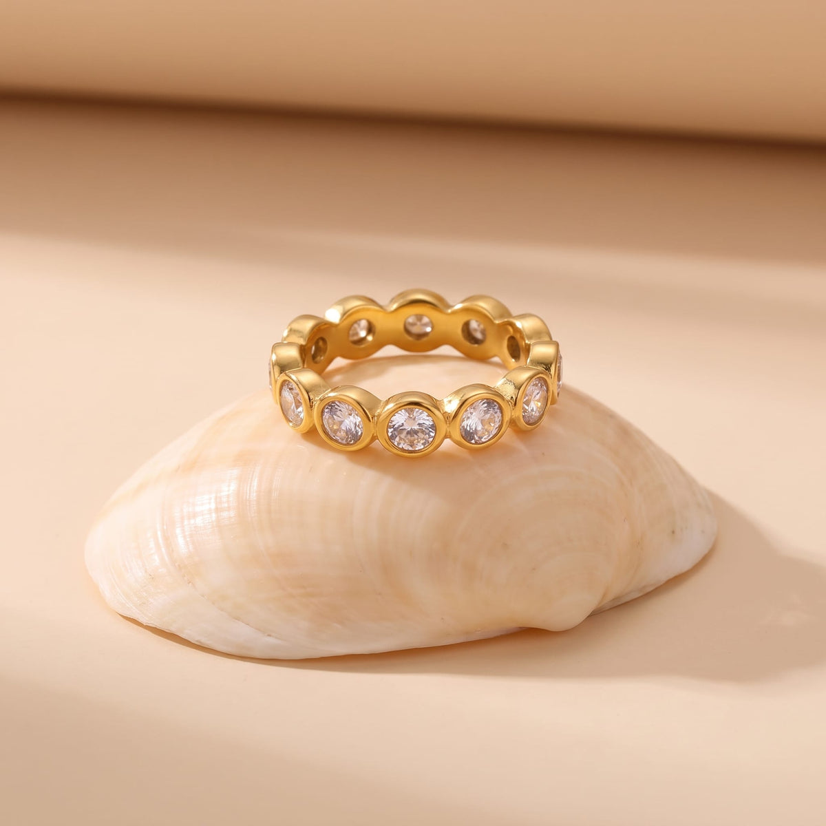 Ariana round eternity gold ring on a seashell against a beige background