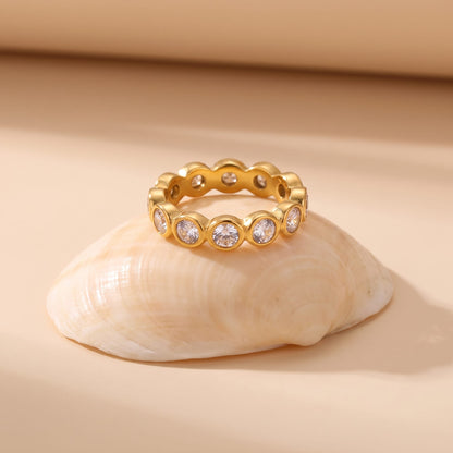 Ariana round eternity gold ring on a seashell against a beige background