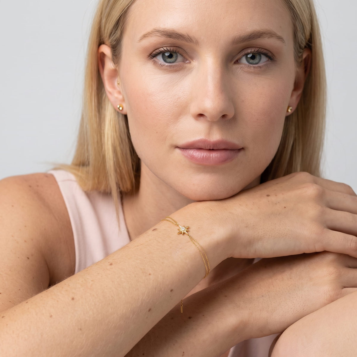 Woman wearing the Astrid north star gold bracelet on the wrist while resting chin on stacked hands