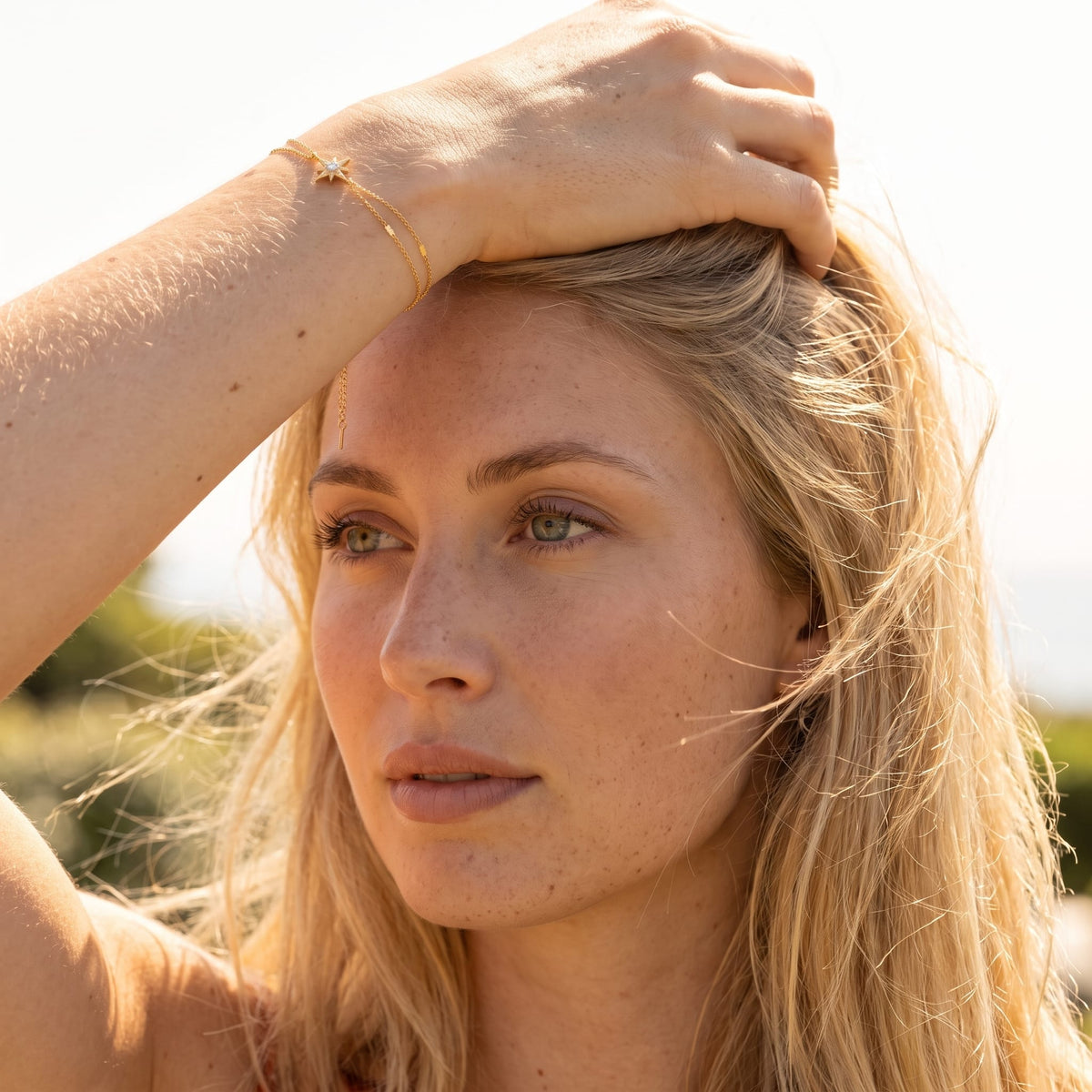 Woman wearing the Astrid north star gold bracelet on the wrist outdoors touching her blonde hair