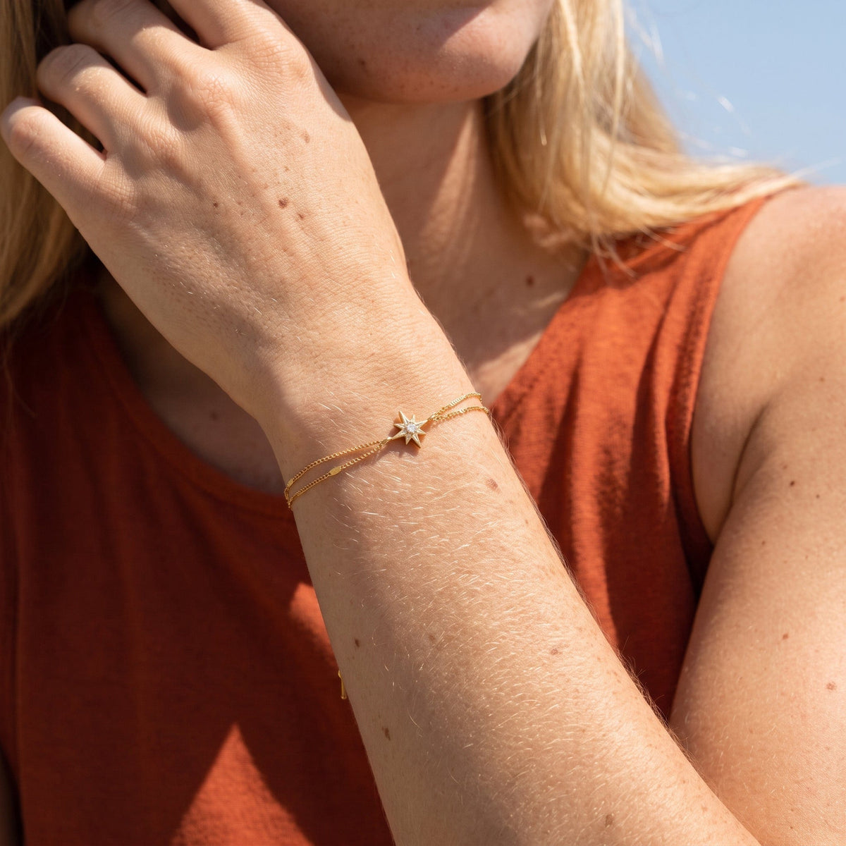 Wider view of a woman wearing the Astrid north star gold bracelet on the wrist, featuring a star charm