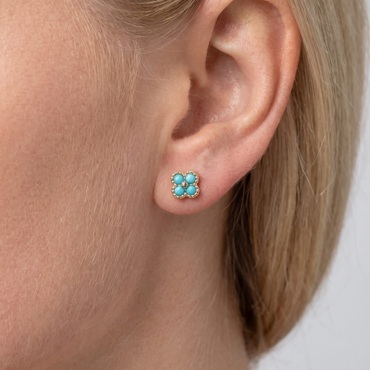 Woman wearing the Aurélie blue stud, a gold clover with four turquoise-blue stones