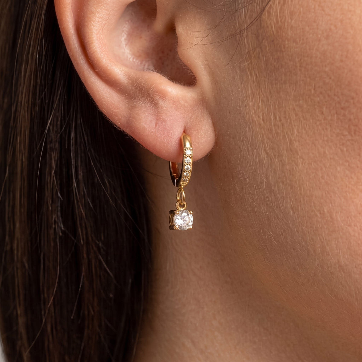 Dark-haired woman wearing an Aurélie gold pavé huggie with a round prong-set crystal drop