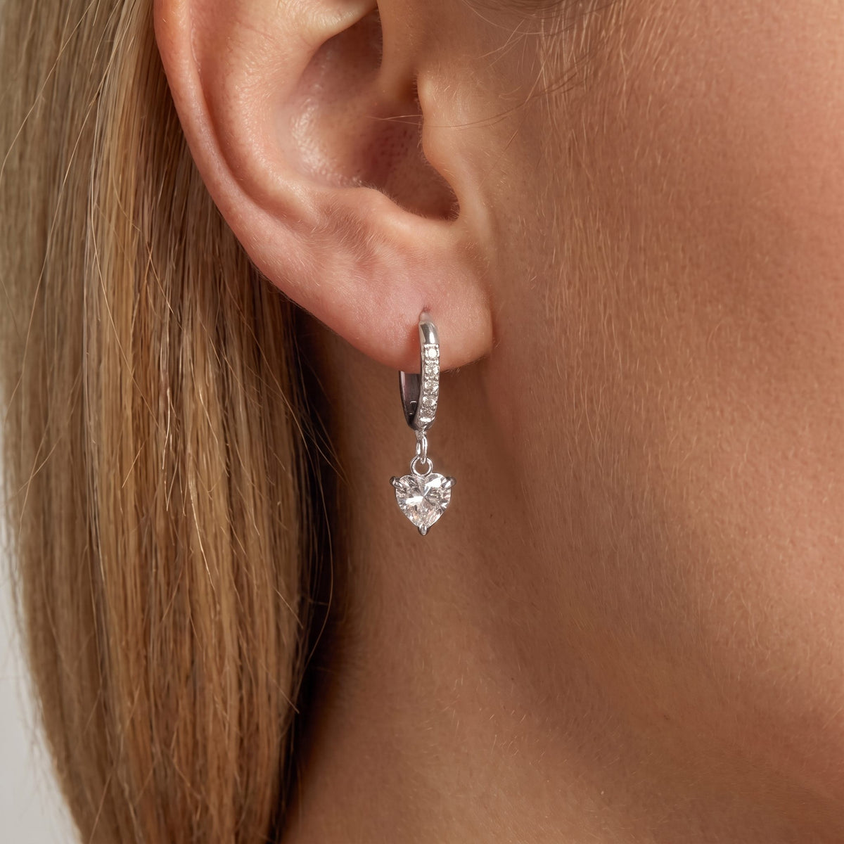 Woman wearing the Aurélie heart earring in silver, a crystal heart hanging from a slim pavé huggie