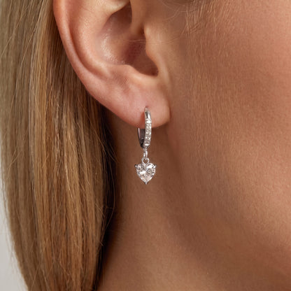 Woman wearing the Aurélie heart earring in silver, a crystal heart hanging from a slim pavé huggie