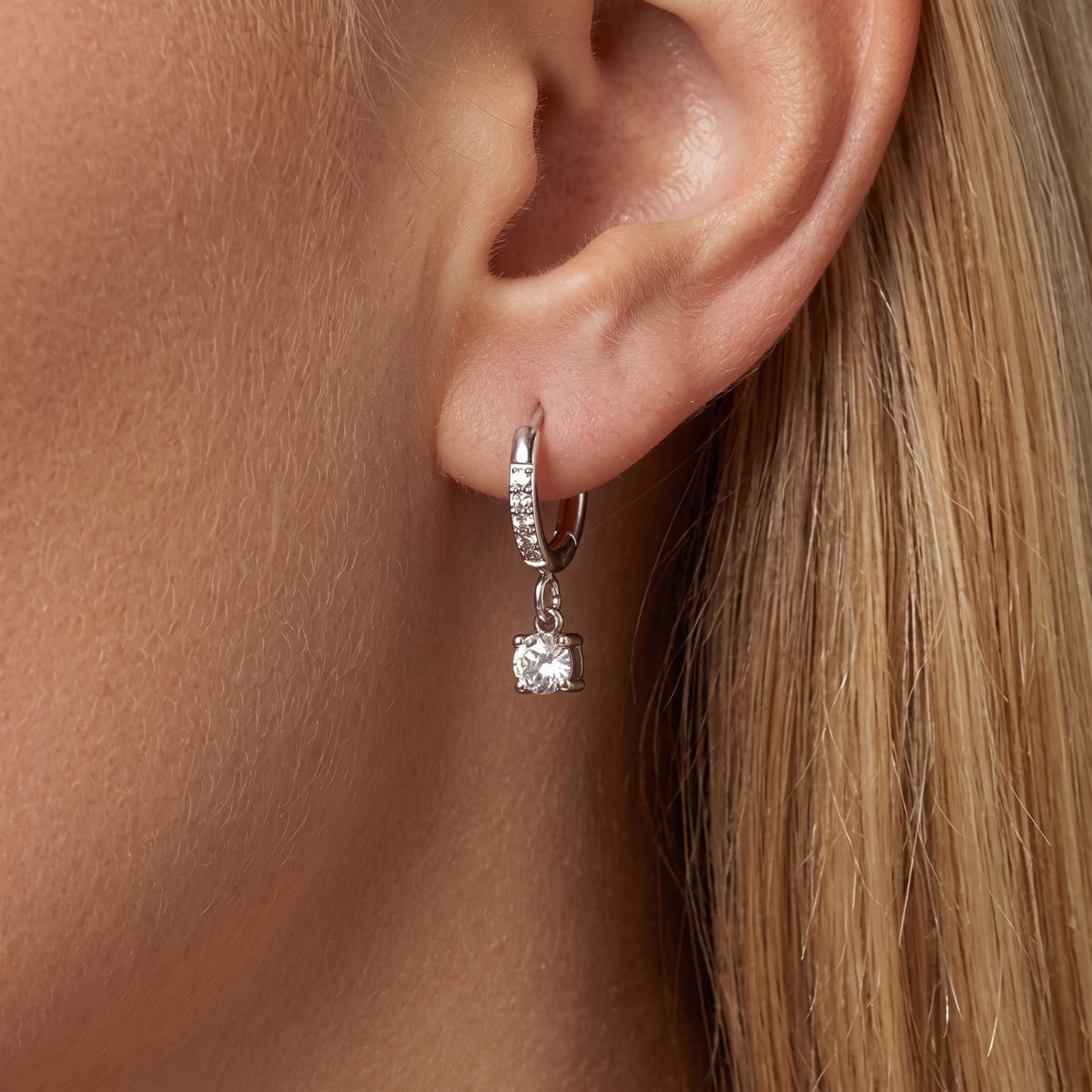 Woman wearing an Aurélie silver huggie with a single round crystal hanging below the lobe
