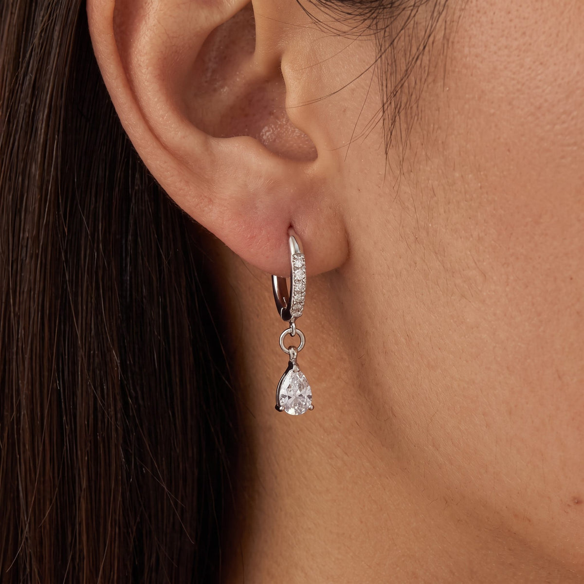 Dark-haired woman wearing an Aurélie silver huggie with a clear pear-shaped crystal drop
