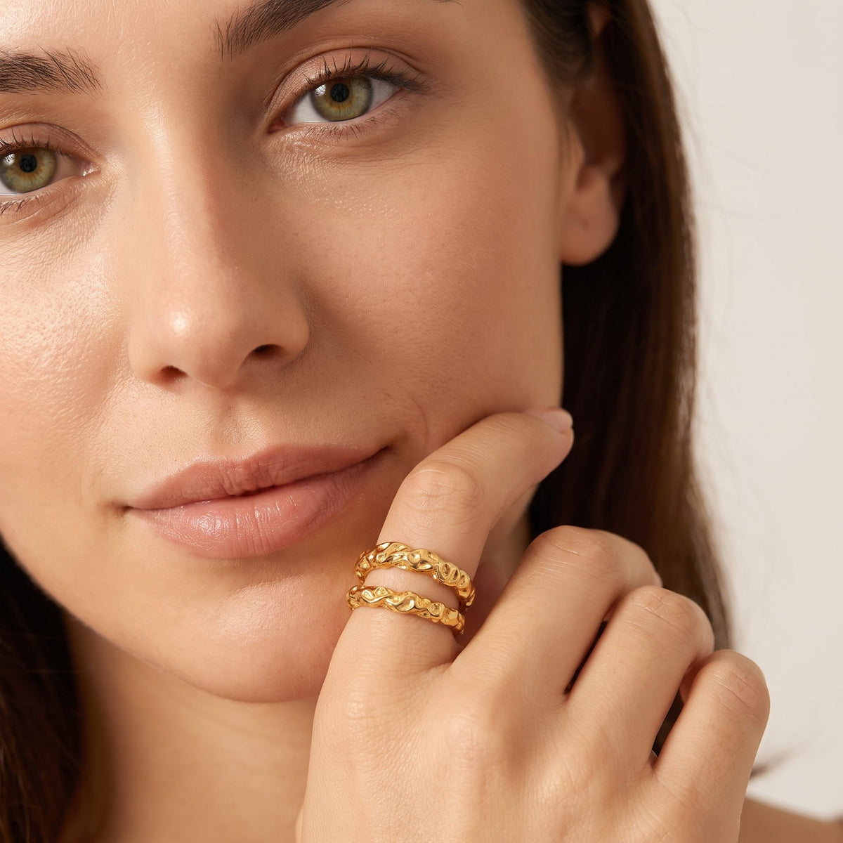 Woman with a fingertip at her lip, wearing the Aurélie hammered double gold ring