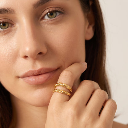 Woman with a fingertip at her lip, wearing the Aurélie hammered double gold ring