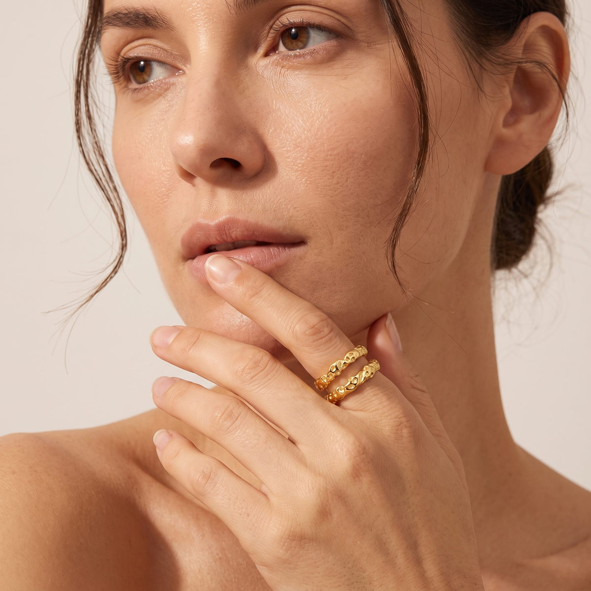 Close-up of a woman's face and hand wearing the Aurélie hammered double gold ring