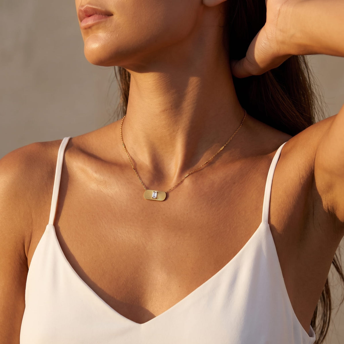 Woman wearing the Aurora sunburst crystal gold necklace at the collarbone while wearing a white camisole