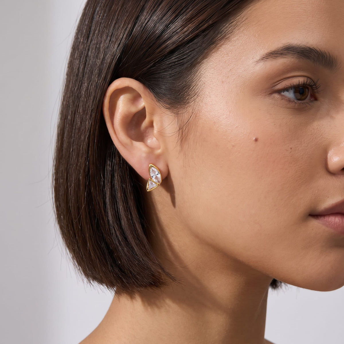 Woman wearing the Aurore crystal wing gold earrings on her earlobe, with dark short hair cropped