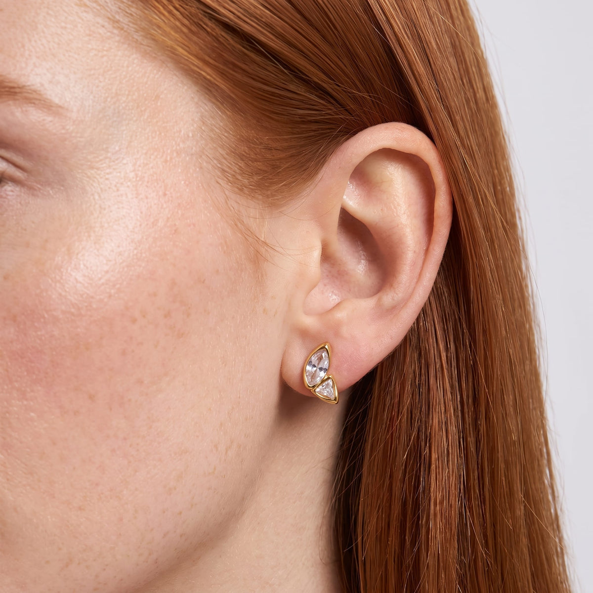 Wider view of a woman wearing the Aurore crystal wing gold earrings on her earlobe, close up on red hair