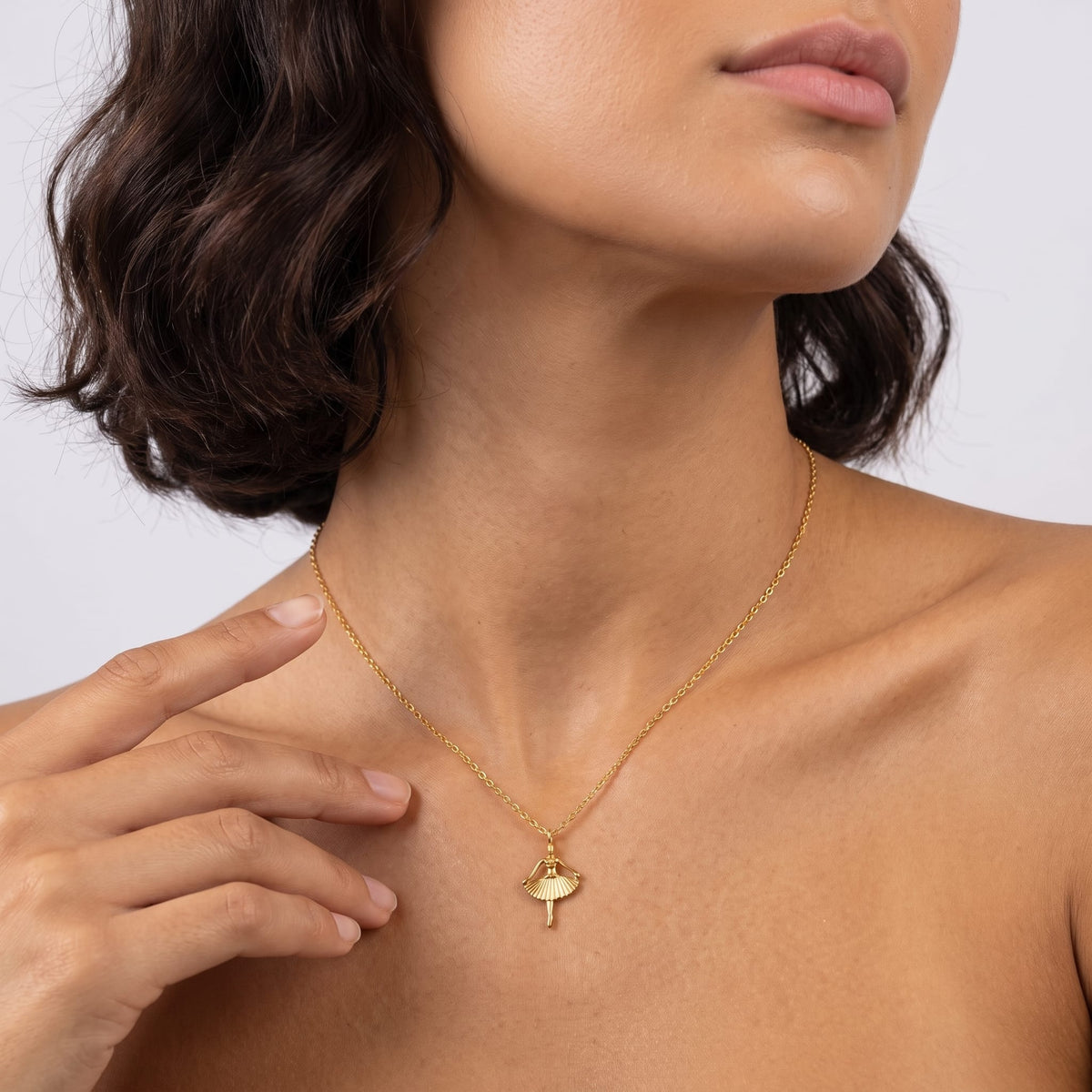 Woman wearing the Ava ballerina gold necklace at the throat with her hand touching her neck