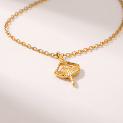 Ava ballerina gold necklace on a white surface with a fine cable chain curved above