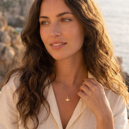 Woman wearing the Ava ballerina gold necklace at the collarbone in a white shirt outdoors