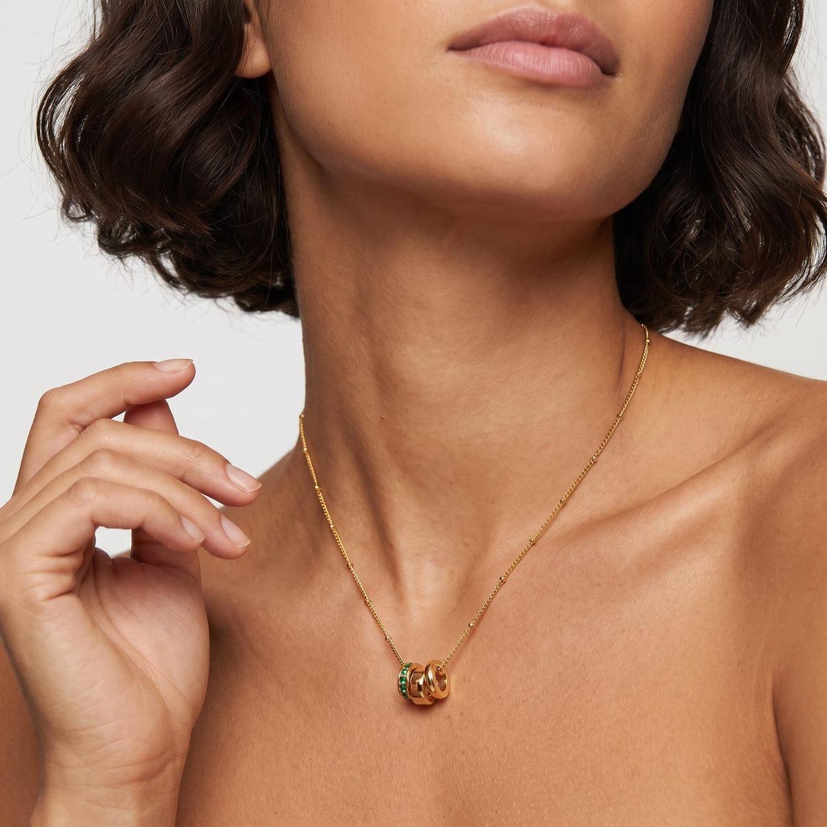 Woman wearing the Benedetta triple ring gold necklace at the collarbone while resting her hand near her chin