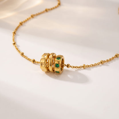 Benedetta triple ring gold necklace on a light surface with soft shadows highlighting the green zircons