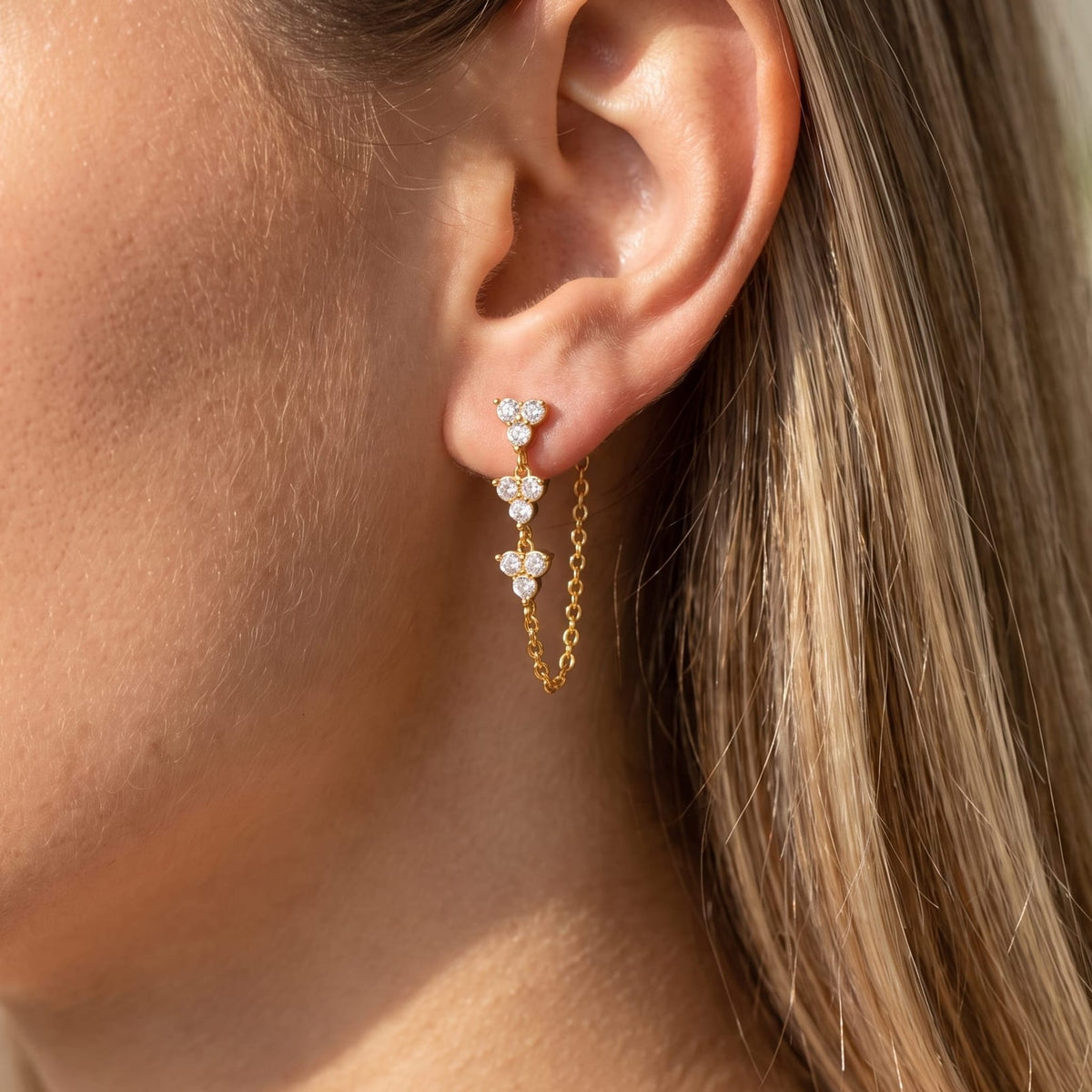 Woman wearing the Bettina crystal cascade gold earrings on her ear close up in warm sunlight