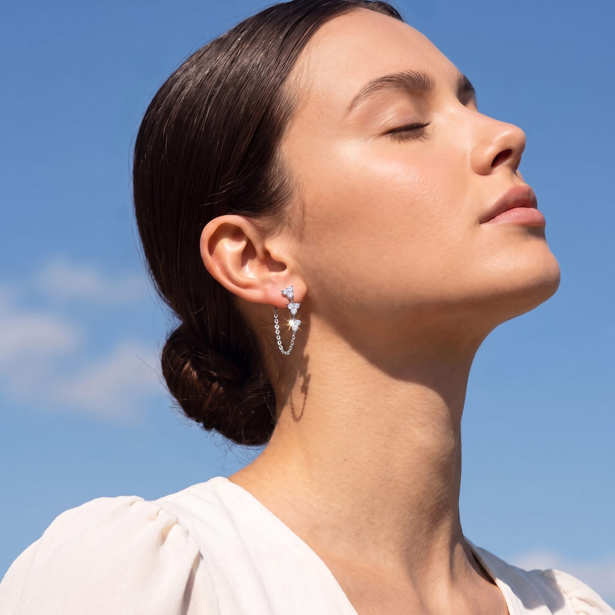 Woman wearing the Bettina crystal cascade silver earrings on her ear against a blue sky