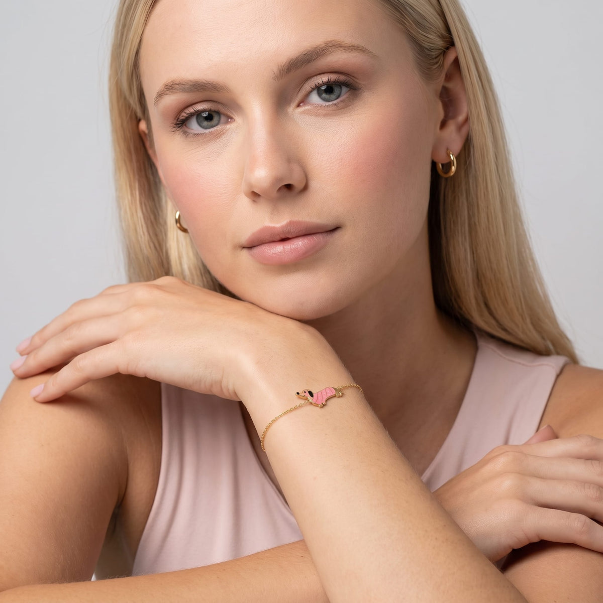 Woman wearing the Bianca pink dachshund gold bracelet on the wrist while resting chin on hand