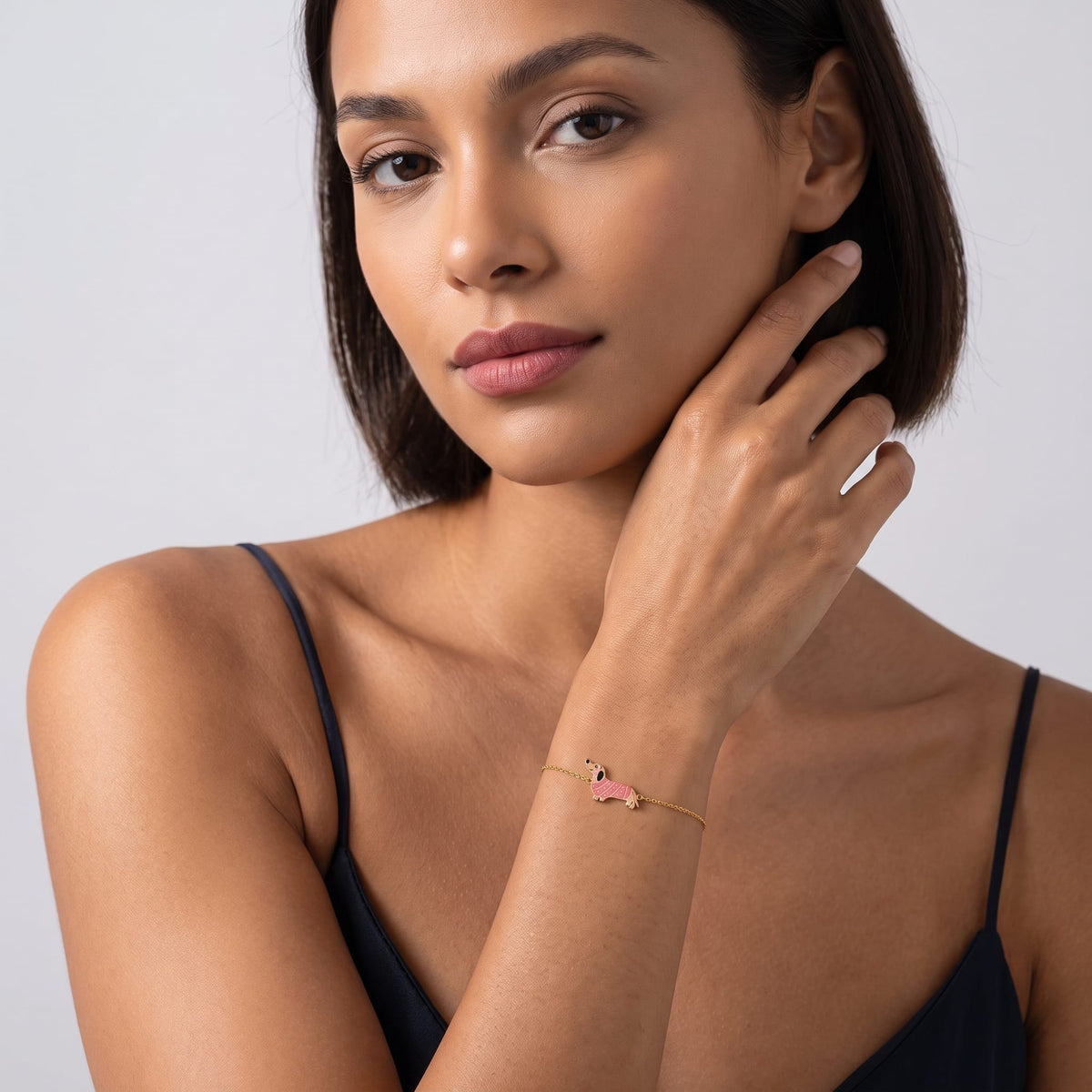Woman wearing the Bianca pink dachshund gold bracelet on the wrist in a black tank top