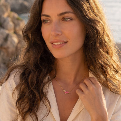Woman wearing the Bianca pink dachshund gold necklace at the collarbone wearing a white linen shirt