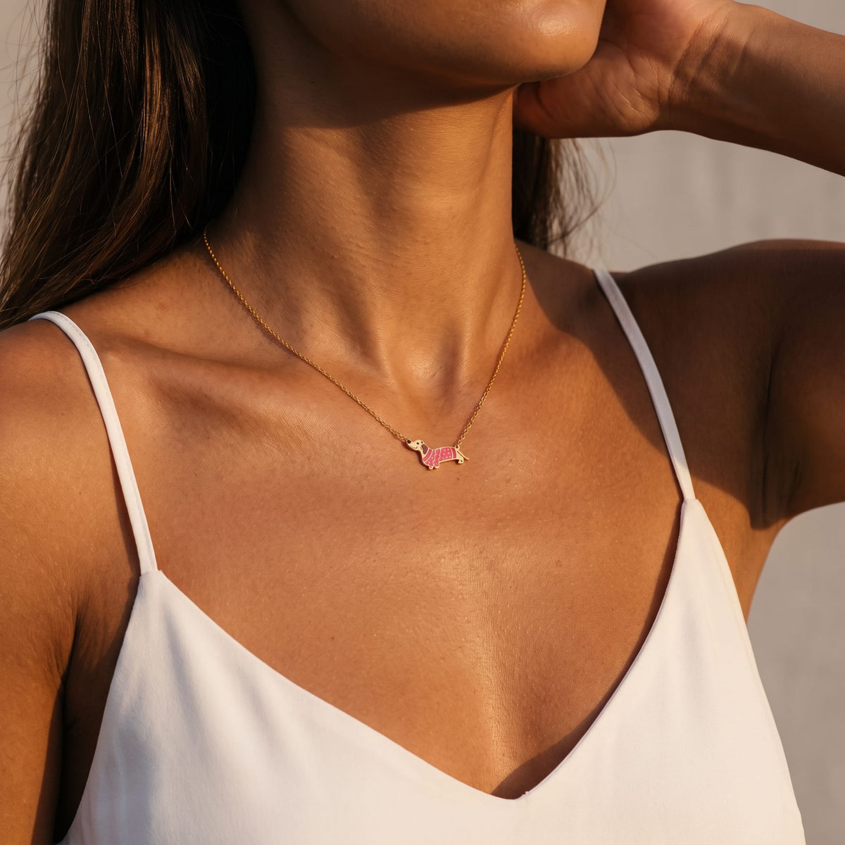 Woman wearing the Bianca pink dachshund gold necklace at the collarbone wearing a white camisole