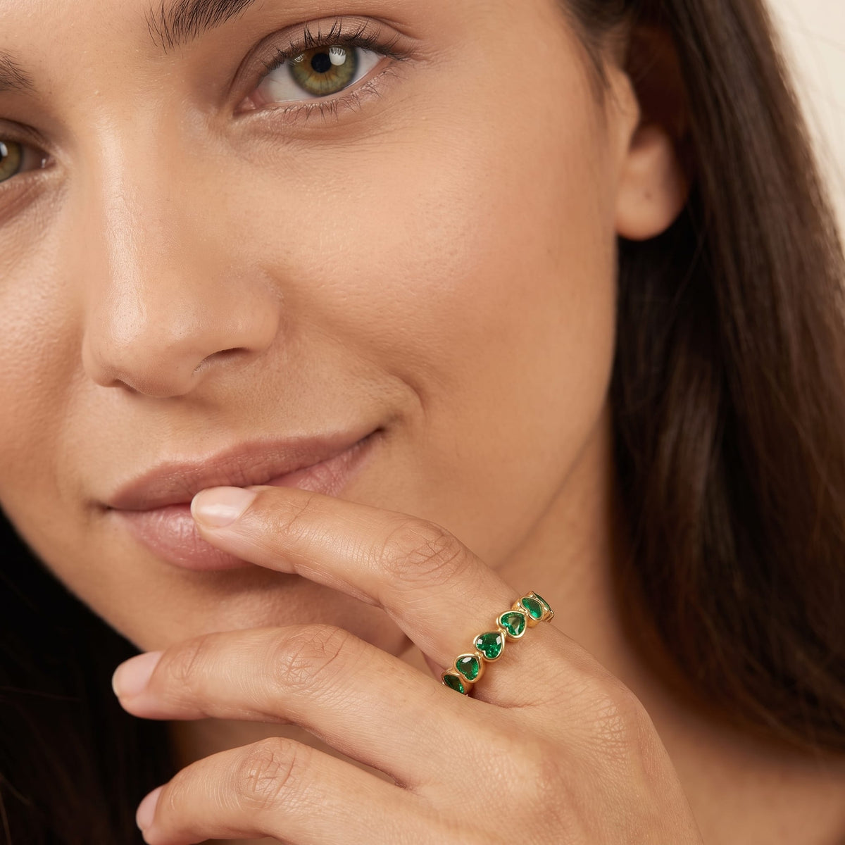 Woman wearing the Camille green heart gold ring on the hand touching her lips