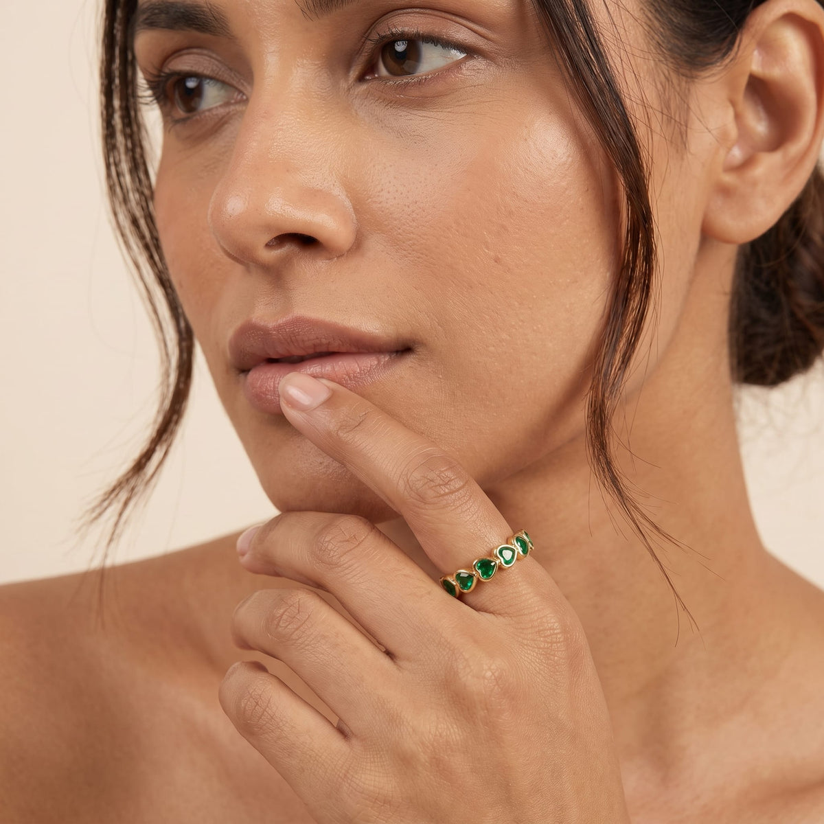 Woman wearing the Camille green heart gold ring on the hand resting near her chin
