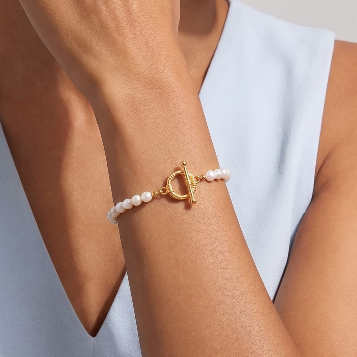 Woman wearing the Camille pearl toggle gold bracelet on the wrist with a blue dress