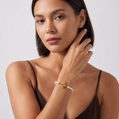 Woman wearing the Camille pearl toggle gold bracelet on the wrist wearing a brown top