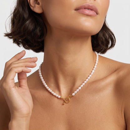 Woman wearing the Camille pearl toggle gold necklace at the throat with short dark hair