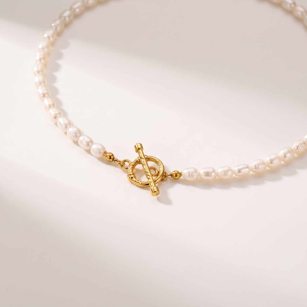 Camille pearl toggle gold necklace on a smooth beige surface