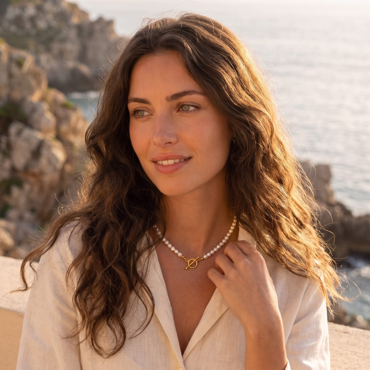 Woman wearing the Camille pearl toggle gold necklace at the collarbone outdoors in a linen shirt
