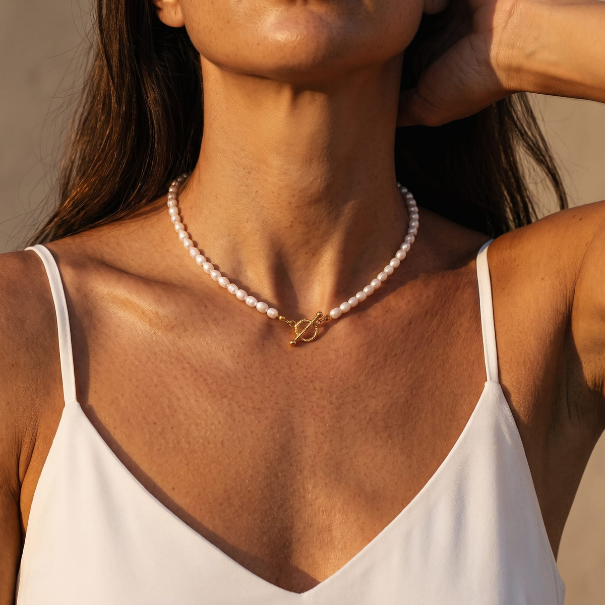 Woman wearing the Camille pearl toggle gold necklace at the collarbone in a white camisole