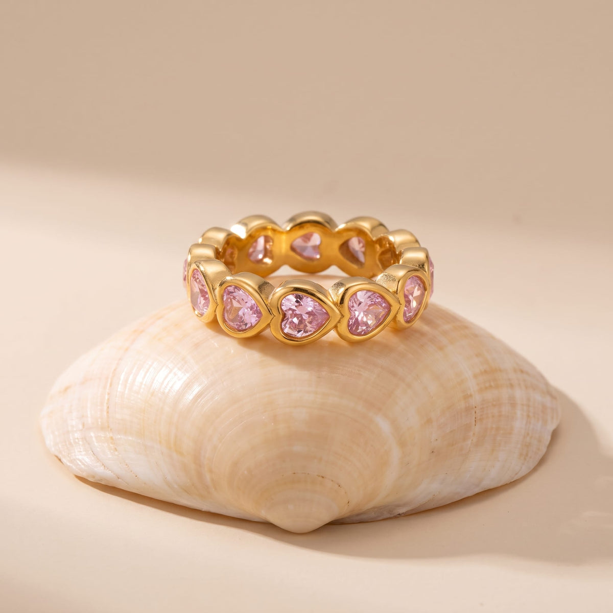 Camille pink heart gold ring on a seashell resting on a beige background
