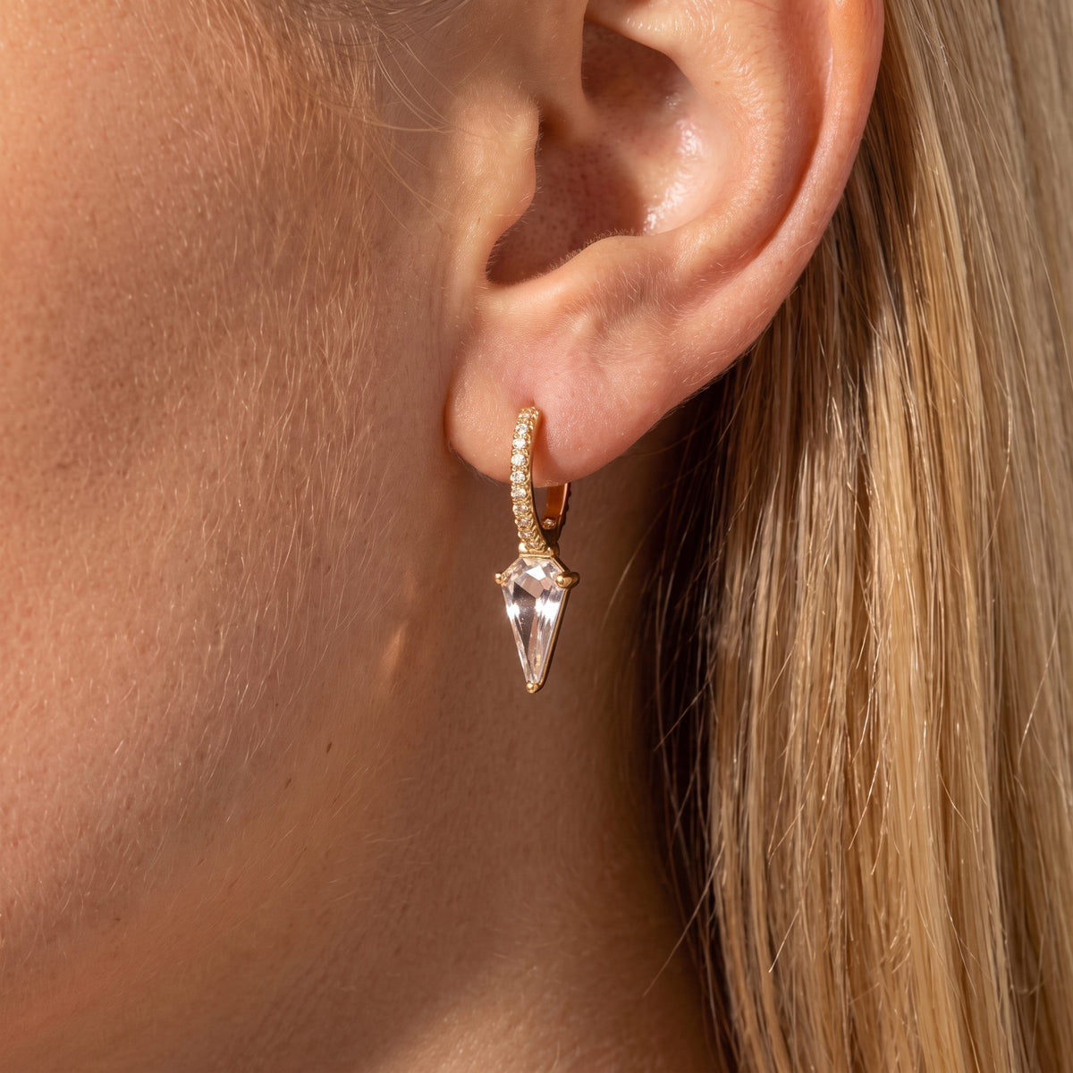 Woman wearing a Camille gold pavé huggie with a long clear crystal prism drop on the ear