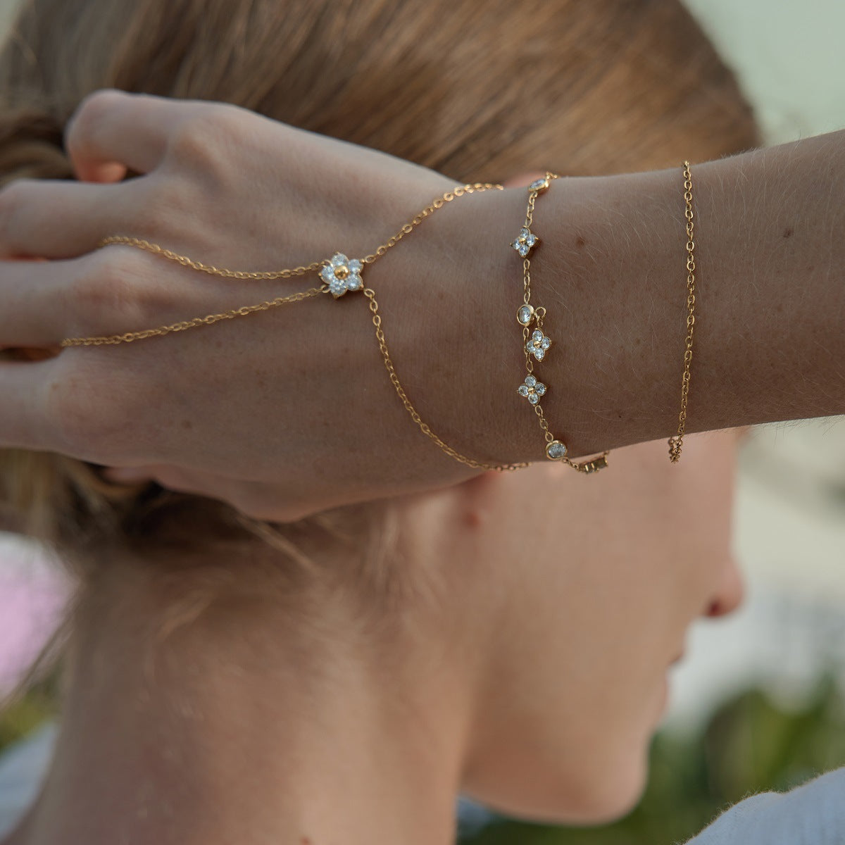 Capucine clover bracelet on a raised wrist next to a hand chain and a fine chain bracelet