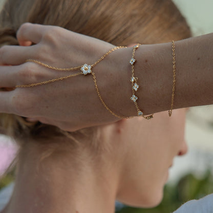 Capucine clover bracelet on a raised wrist next to a hand chain and a fine chain bracelet