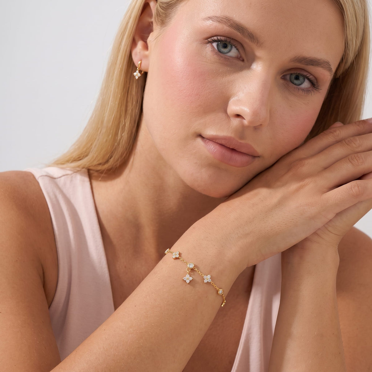 Woman wearing the Capucine clover drop gold bracelet on the wrist while resting her cheek on stacked hands