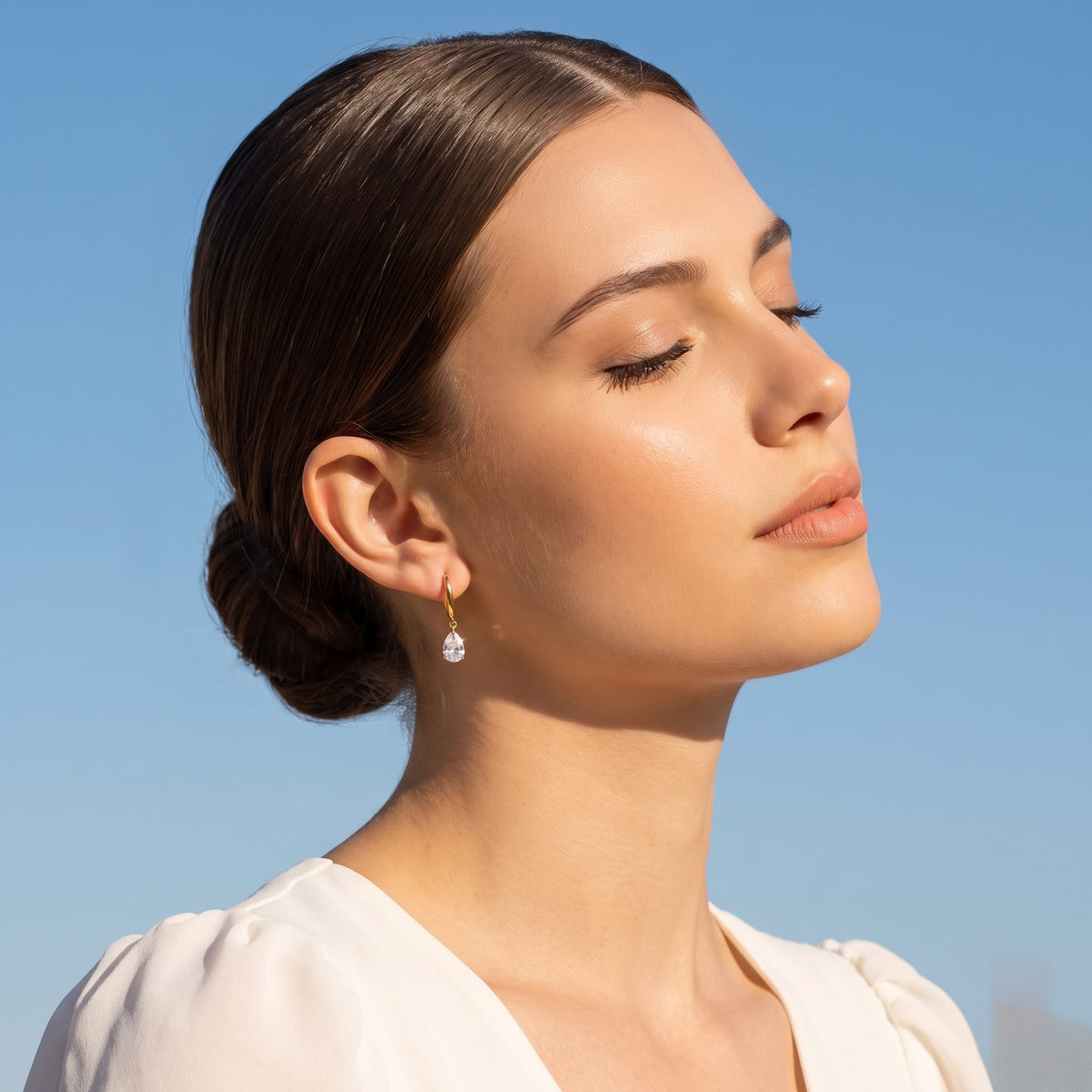 Woman wearing the Carla teardrop huggie gold earrings on the ear with eyes closed in sunlight