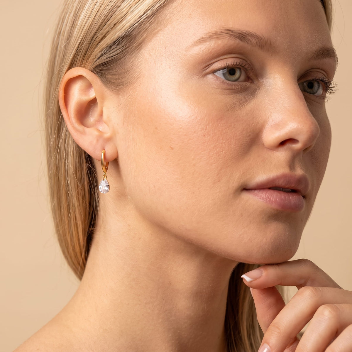 Woman wearing the Carla teardrop huggie gold earrings on the ear resting hand near her chin