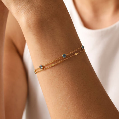 Woman wearing the Cécile blue crystal gold bracelet on the wrist, wearing a white top