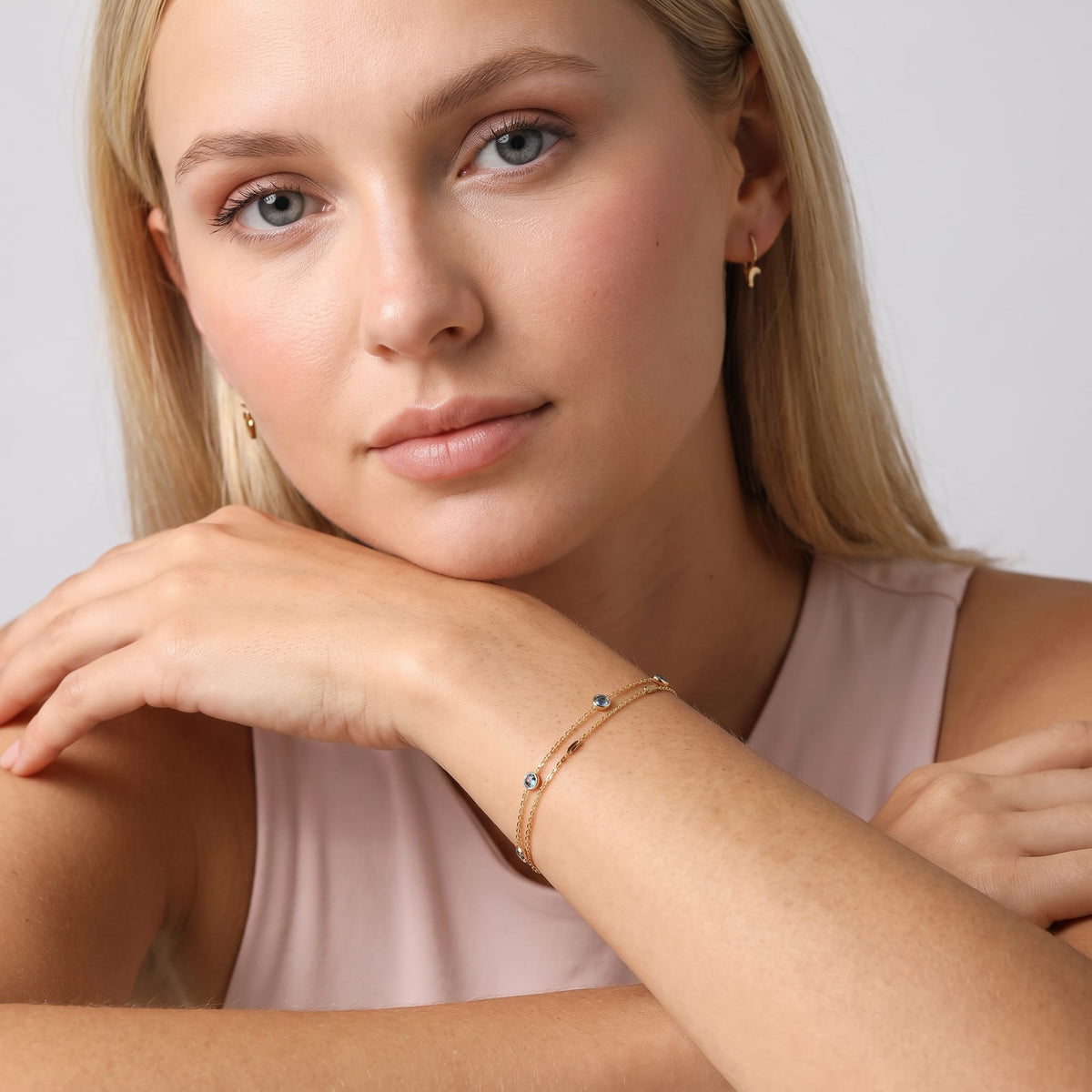 Woman wearing the Cécile blue crystal gold bracelet on the wrist while resting chin on hand