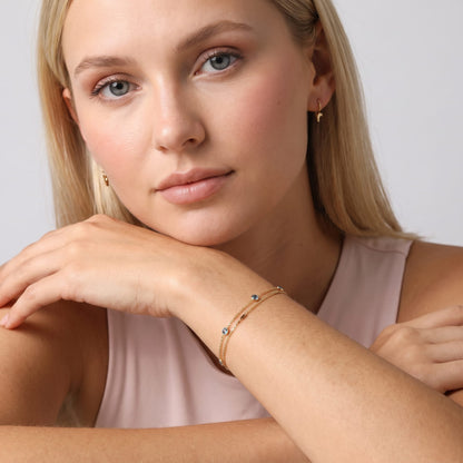 Woman wearing the Cécile blue crystal gold bracelet on the wrist while resting chin on hand