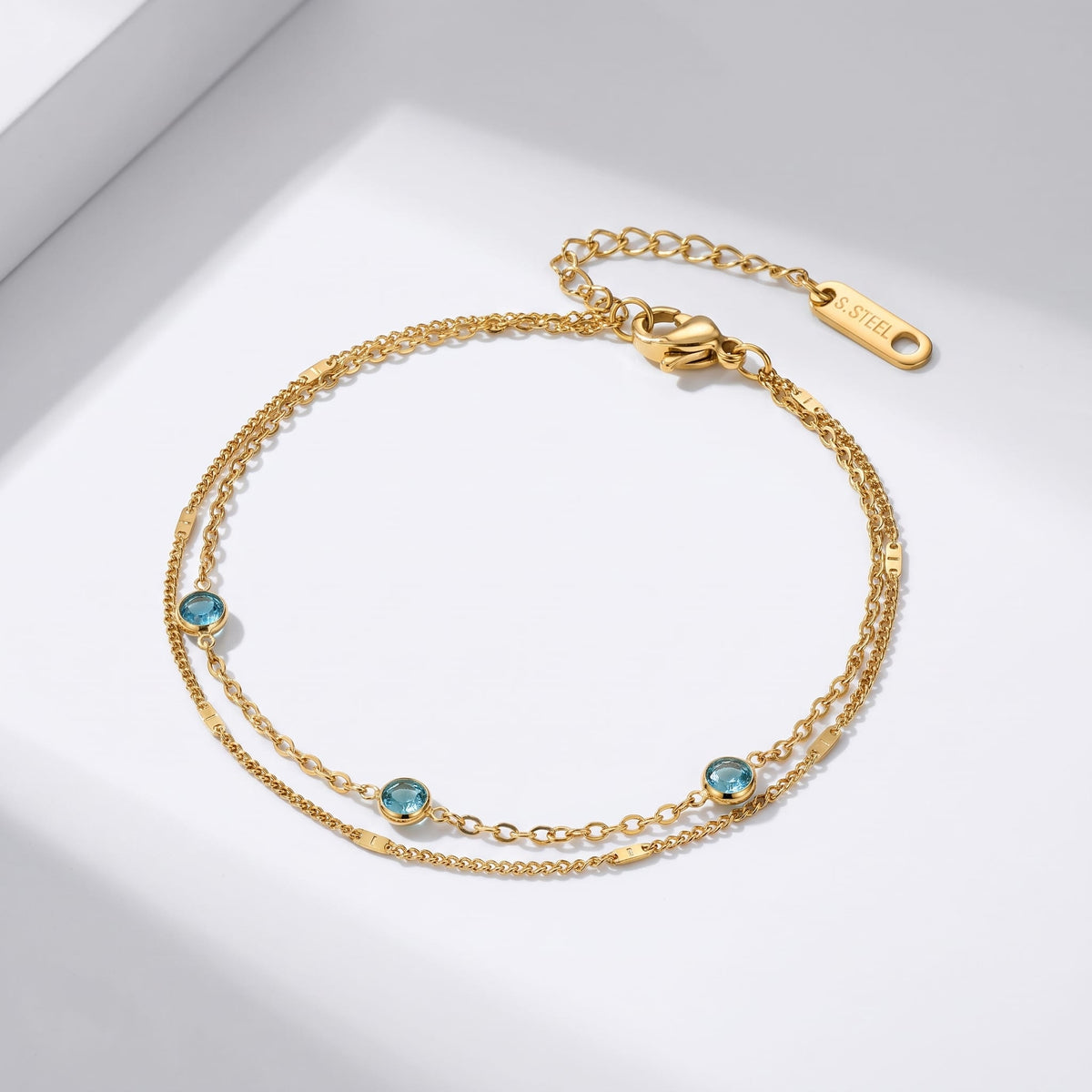 Cécile blue crystal gold bracelet on a white surface showing double chain and blue zircons