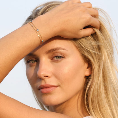 Woman wearing the Cécile blue crystal gold bracelet on the wrist touching her blonde hair