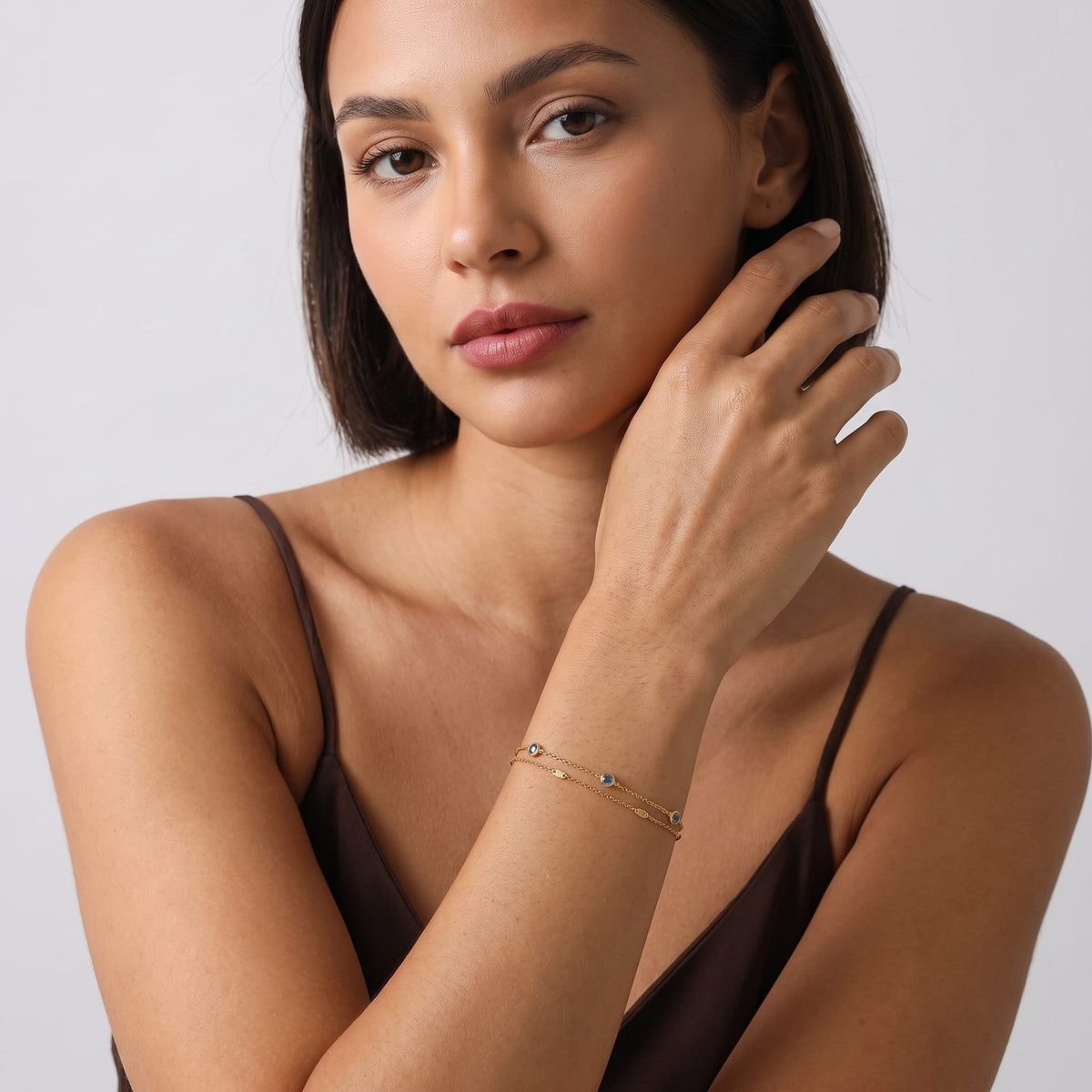 Woman wearing the Cécile blue crystal gold bracelet on the wrist in a dark brown top